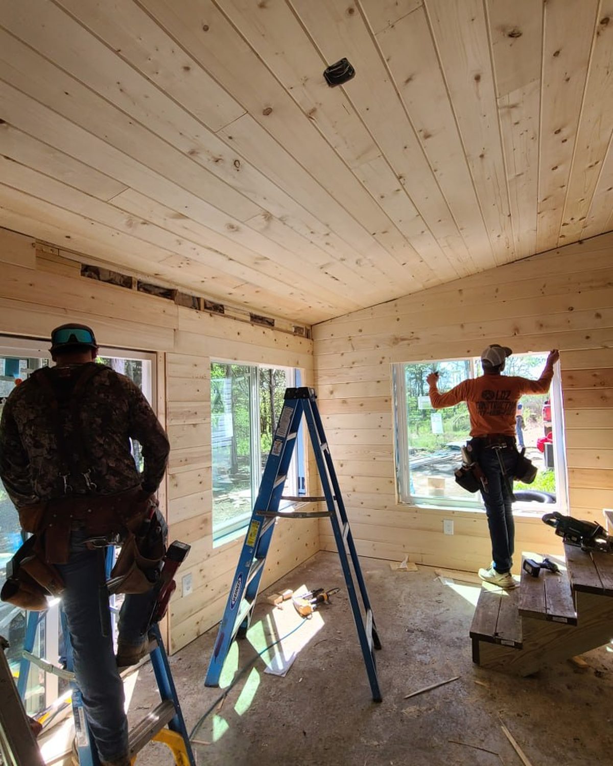 Two L.O.Z. Construction crew members installing windows in a pine-lined sunroom