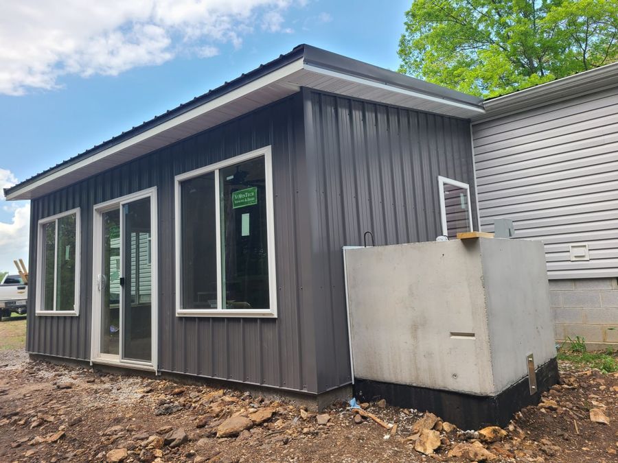 Dark metal-sided sunroom addition with the concrete storm shelter beside it