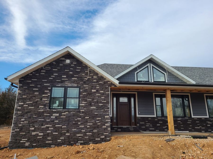 Stone-front custom home with a dark front door, triangle gable windows and timber porch posts