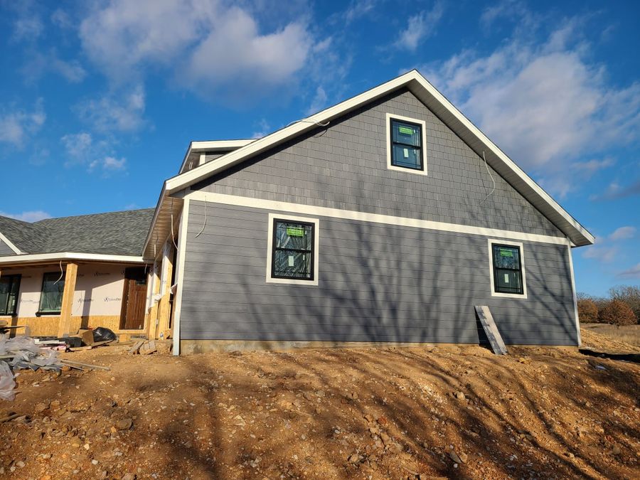 Gable end of a gray-sided custom home with shake accents under a blue sky
