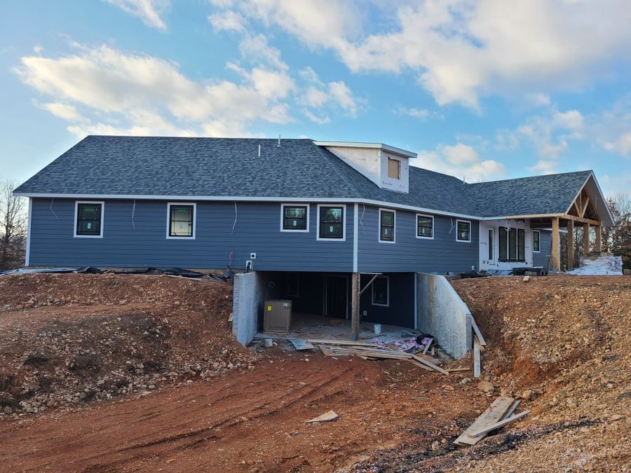 Rear of a gray-sided custom home with a walk-out basement on a graded rural lot