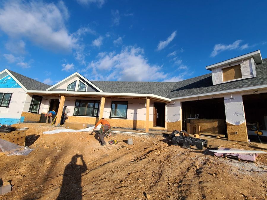 House-wrapped custom home with shingles on and timber porch posts, crew working out front