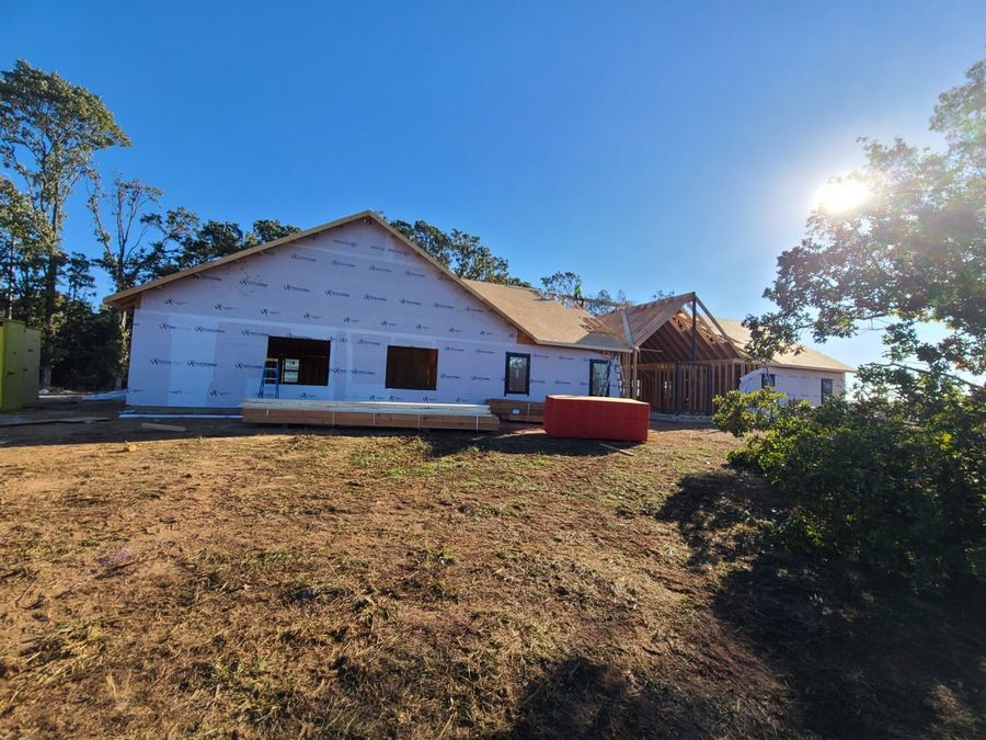 House-wrapped custom home mid-build on a sunny day with lumber stacked outside