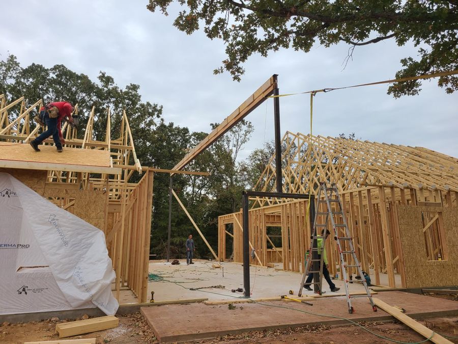Steel beam being set among roof trusses by the L.O.Z. Construction framing crew