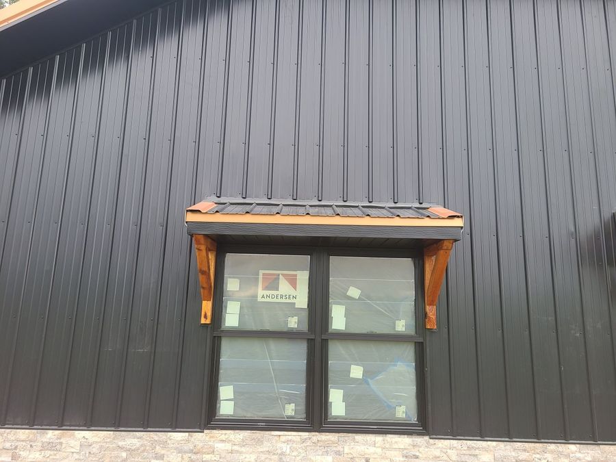 Window with a timber bracket awning on black metal siding over a stone wainscot