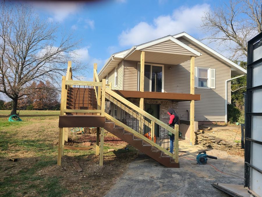 New deck stairs and railing going up on a rural home with a crew member working below