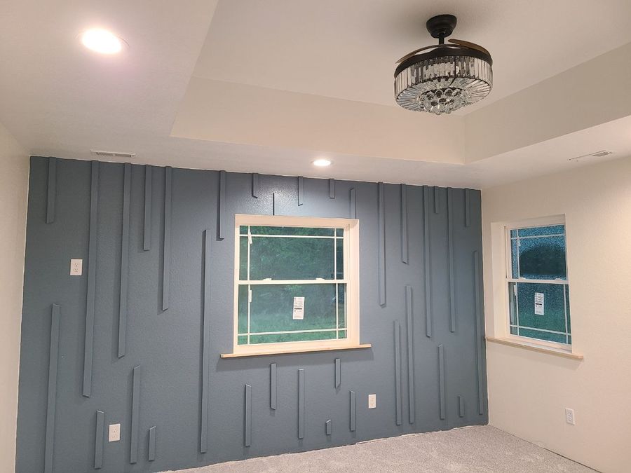 Finished blue accent wall with vertical trim pieces and a crystal ceiling fan light