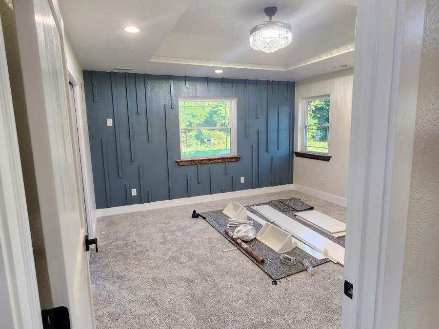 Bedroom seen through the doorway with a blue accent wall, tray ceiling and chandelier fan