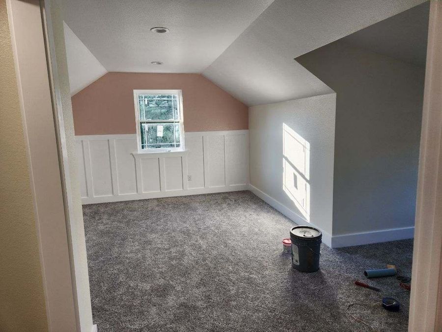 Upstairs bedroom with a sloped ceiling, white board-and-batten wainscot and new carpet