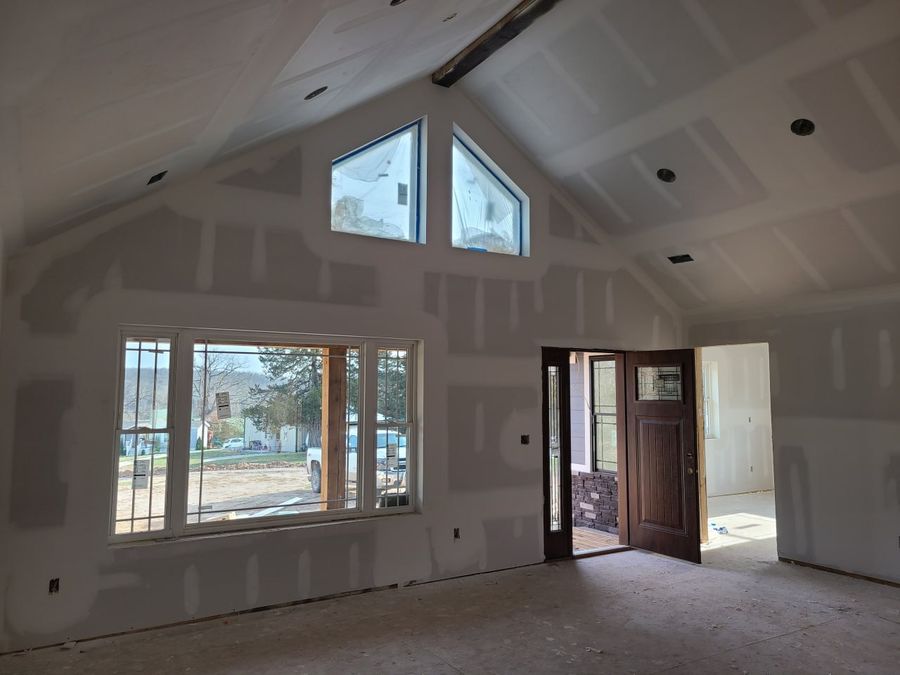 Vaulted great room at the drywall stage with triangle windows and the front door open