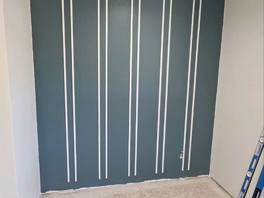 Green accent wall with white vertical trim strips in a bedroom under construction