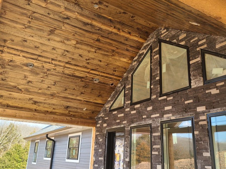 Stained tongue-and-groove pine porch ceiling above stone veneer and black-framed windows