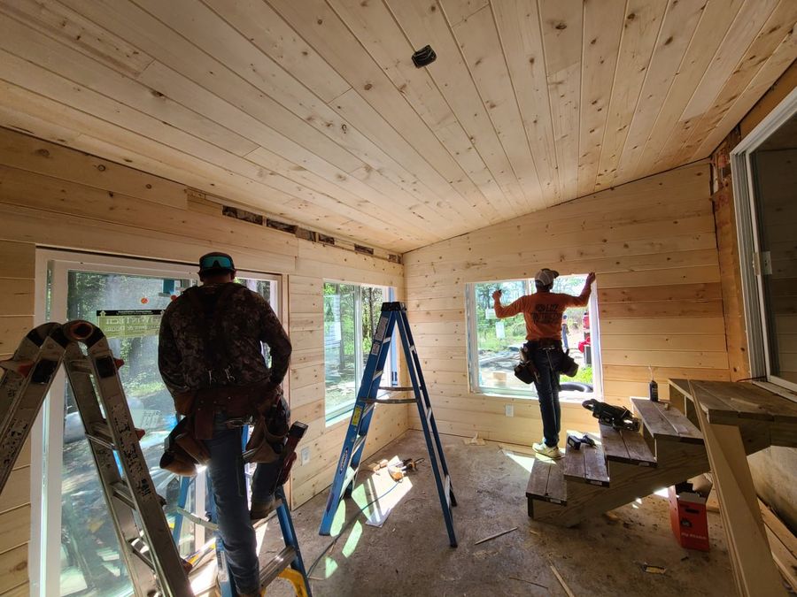 Two L.O.Z. Construction crew members installing windows in a pine-lined sunroom
