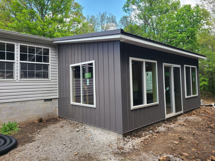Finished dark metal-sided sunroom addition with white windows and a sliding door