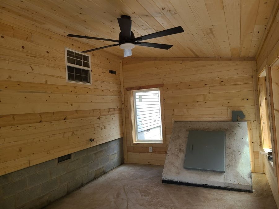 Finished pine sunroom interior with a ceiling fan and the storm shelter door