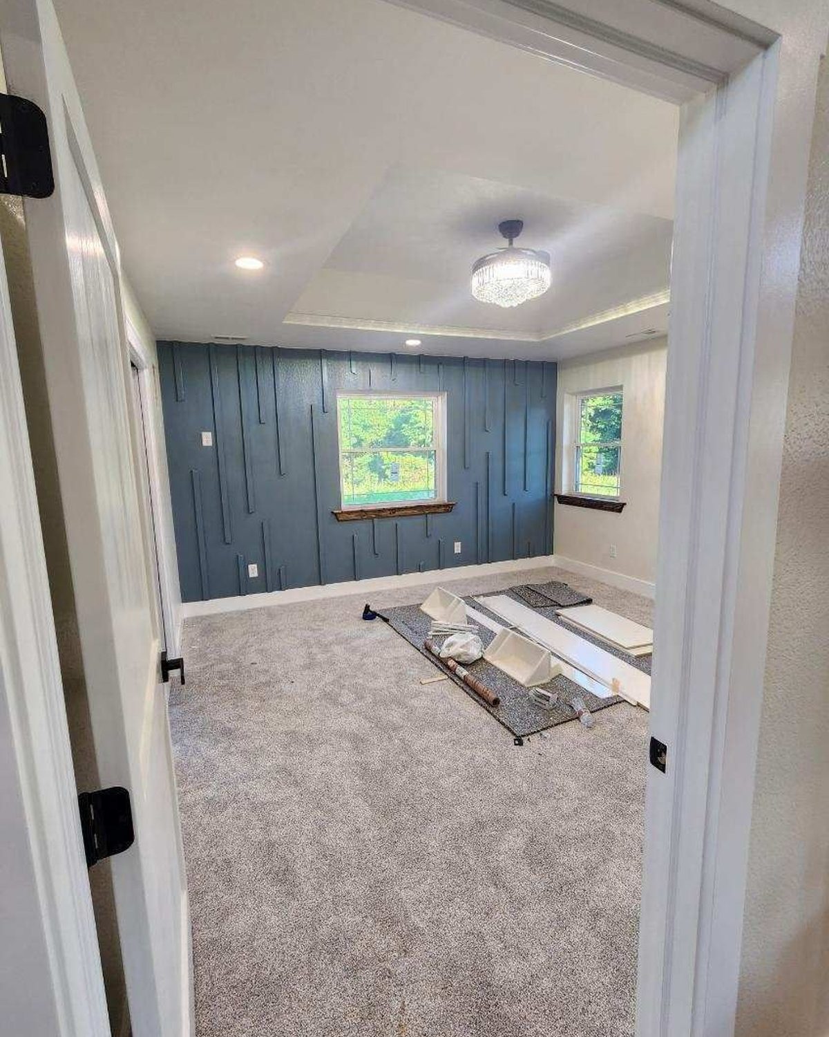 Finished bedroom with a blue accent wall, tray ceiling and chandelier fan in a custom home