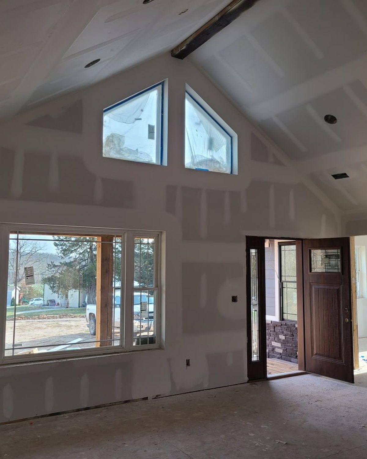 Vaulted great room at the drywall stage with triangle windows and the front door open